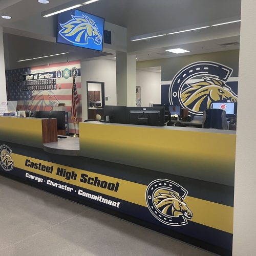 The front office of Casteel High School, featuring the school logo, desks, and the words "Courage • Character • Commitment" on the yellow and blue front counter.