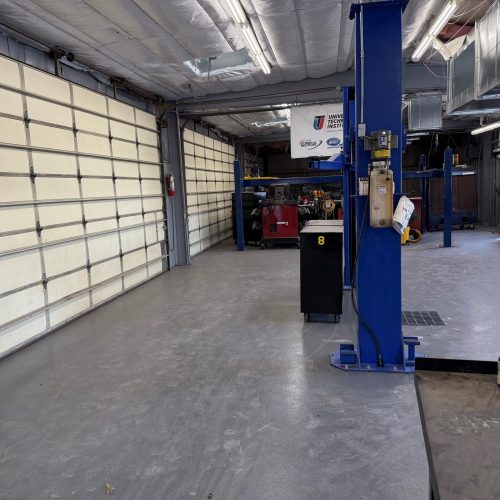 Automotive repair shop with a lift, garage doors, workbenches, and various tools visible in a clean, organized space.